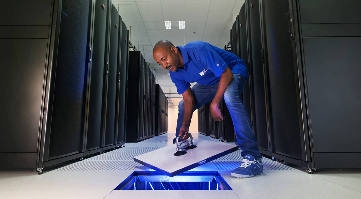 Een technicus inspecteert het vloerpaneel in een gangpad van een datacenter tussen serverrekken.